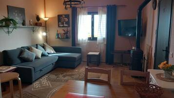 Een woonkamer met een bank, een televisie, een open haard en een eethoek met een tafel en stoelen.
