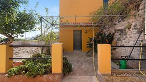 A yellow building with a door, a small garden with plants, and a hose.
