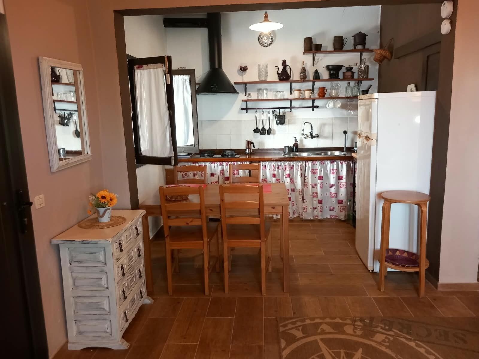 Una cucina con mobili in legno, un tavolo da pranzo con sedie, un frigorifero e una finestra con tende.