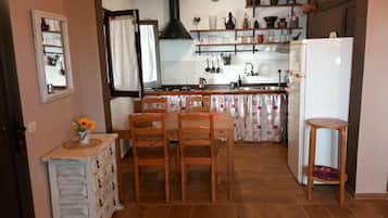Una cucina con mobili in legno, un tavolo da pranzo con sedie, un frigorifero e una finestra con tende.