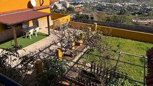 A yellow building with a terrace, a view of the sea, and a garden.