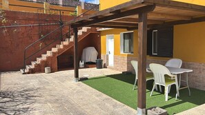 Un'area esterna riparata con tavolo e sedie da patio, una scala e una porta che dà su un edificio.