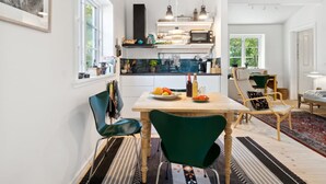 A modern kitchen with a dining area, featuring a wooden table, green chairs, and a striped rug.
