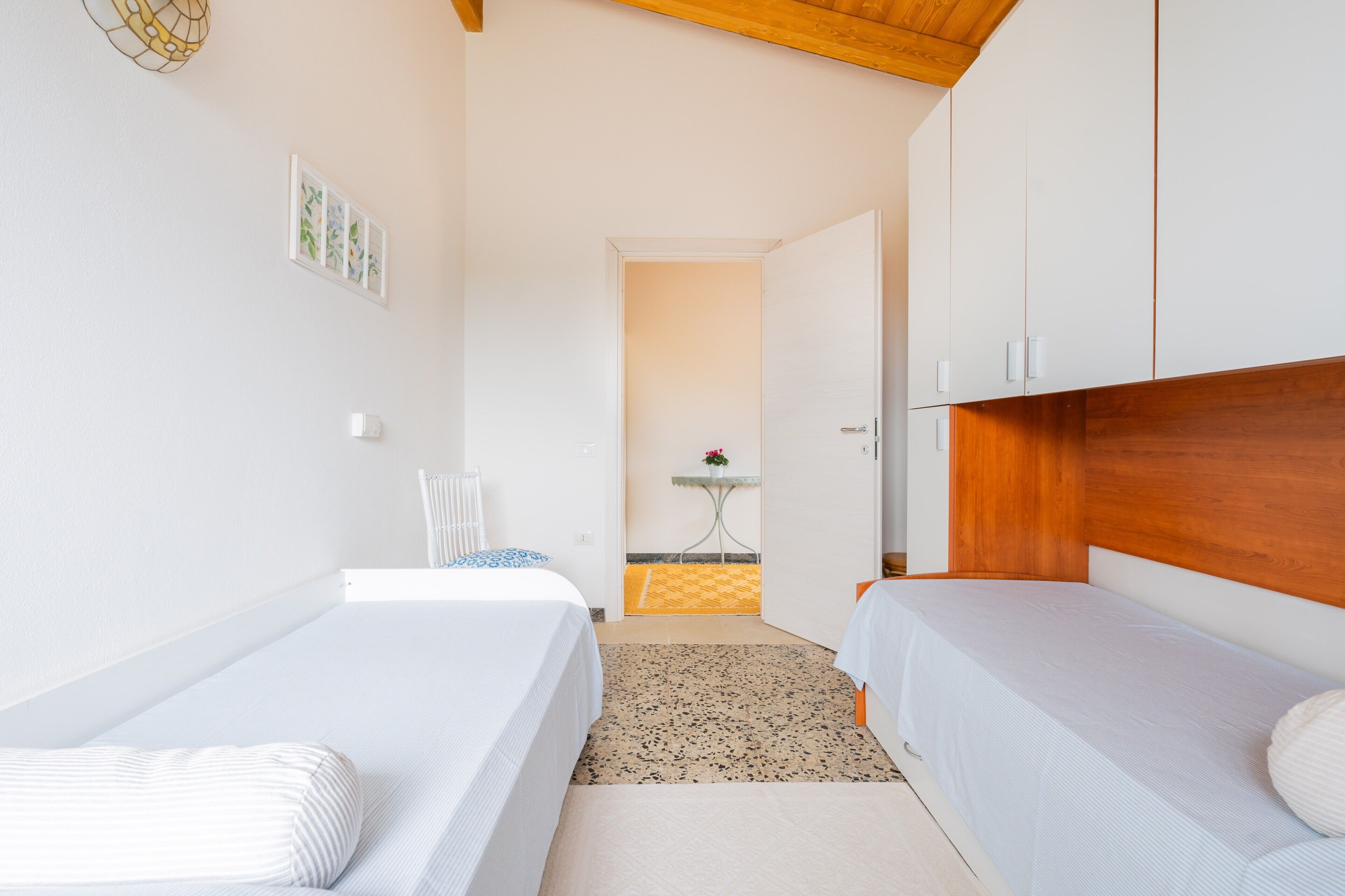 A room with two beds, a small table with a plant, and a door leading to another room.