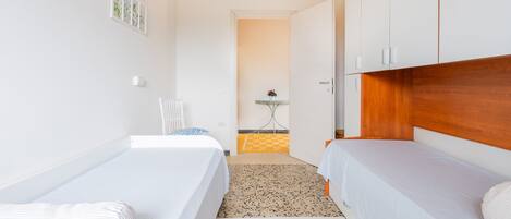 A room with two beds, a small table with a plant, and a door leading to another room.