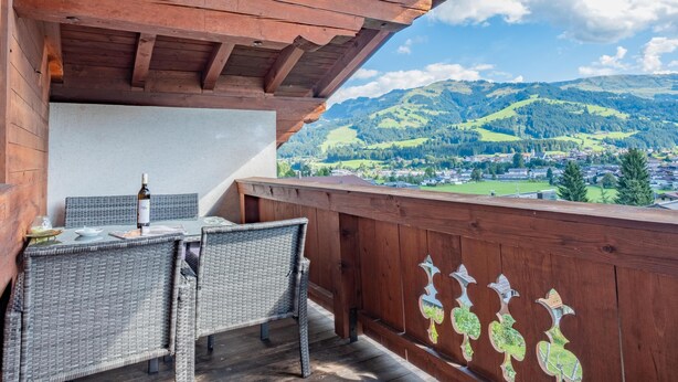 Een houten balkon met rieten meubilair en uitzicht op een stad en bergen.