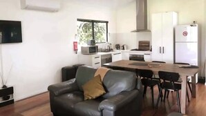 A modern kitchen with white cabinets, a dining table, and a black leather sofa. - Blacksmith Corner (Nannup)