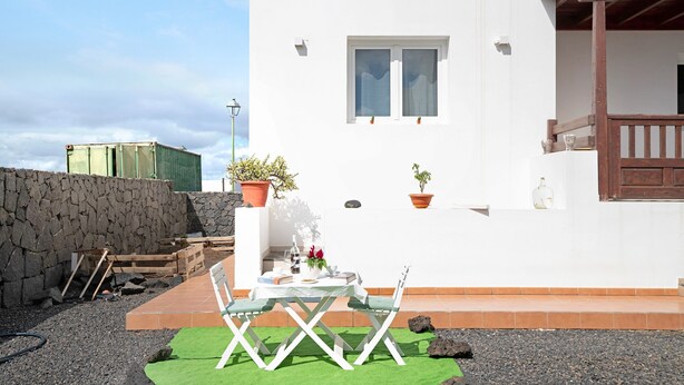 Un bâtiment blanc doté d’un balcon, une table avec des chaises et des plantes en pot.