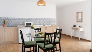 Une cuisine moderne avec un coin repas, comprenant une table ronde en verre, des chaises, un luminaire suspendu et un revêtement mural en carreaux.