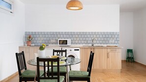 Une cuisine compacte avec une table à manger en verre, des chaises en bois, un four à micro-ondes et un lave-linge.