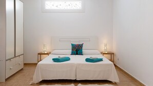 Une chambre à coucher comprenant un lit, deux tables de chevet, une armoire et une fenêtre agrémentée d’un cadre décoratif.