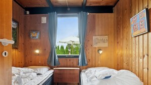 Una habitación tipo cabaña con dos camas, techo de madera, una ventana con cortinas y una mesita.