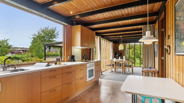 Cocina moderna con armarios de madera, una isla central y una zona de comedor con mesa y sillas.