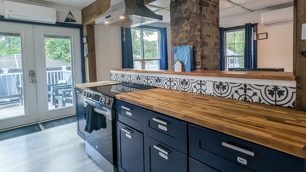 A modern kitchen with a wooden countertop, dark cabinets, and a large window. - Modern Downtown Escape HotTub Fire Pit Games 12ppl (Keene)