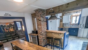 A modern kitchen with a wooden table and benches, a brick column, and a view of the living area. - Modern Downtown Escape HotTub Fire Pit Games 12ppl (Keene)