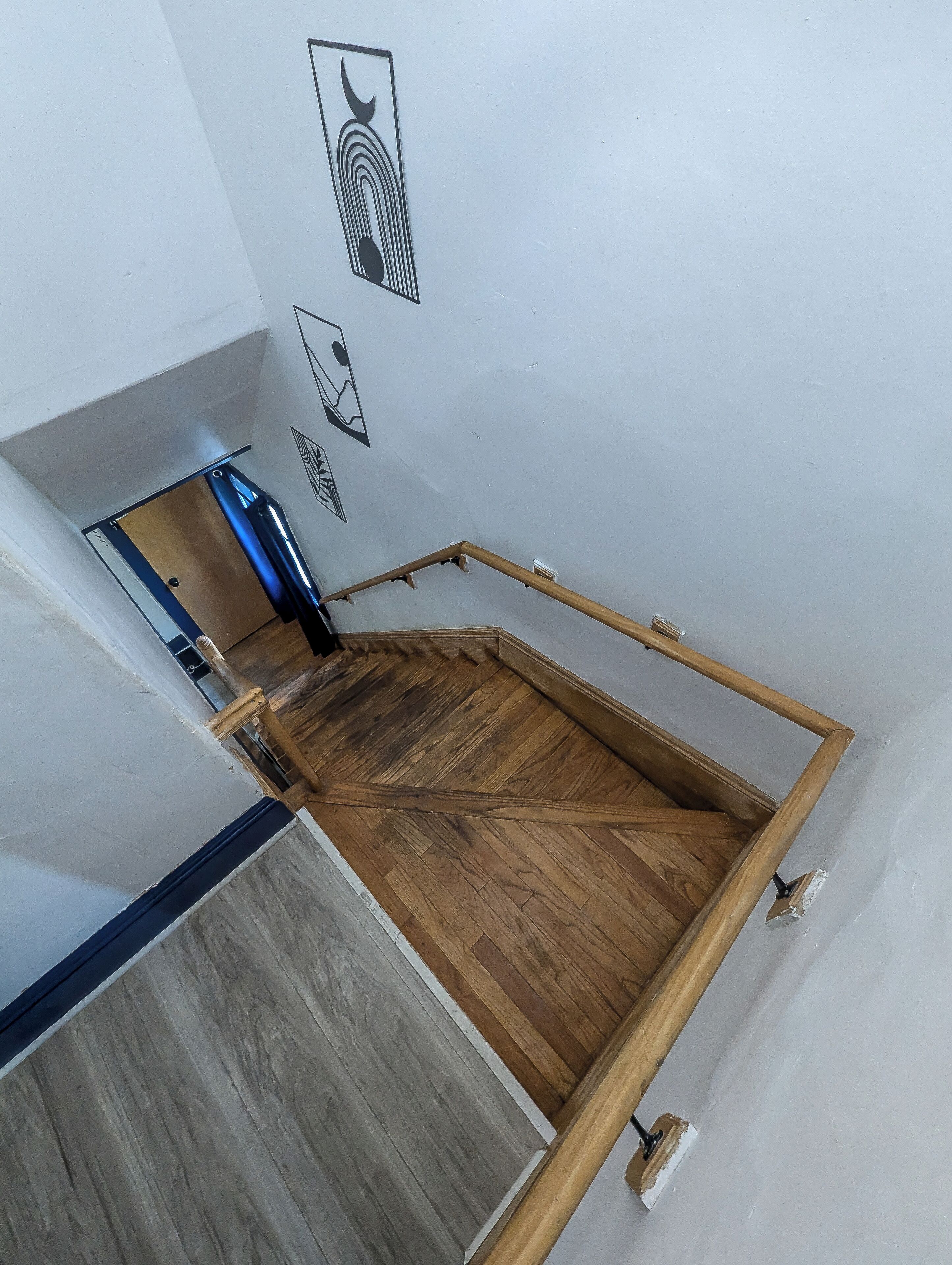 Una habitación con piso de madera, estructura de cama de metal y pared blanca con un ventanal pequeño.