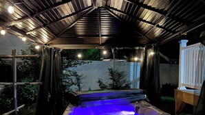 A hot tub under a covered patio with a wooden deck and a metal railing. - Modern Downtown Escape HotTub Fire Pit Games 12ppl (Keene)