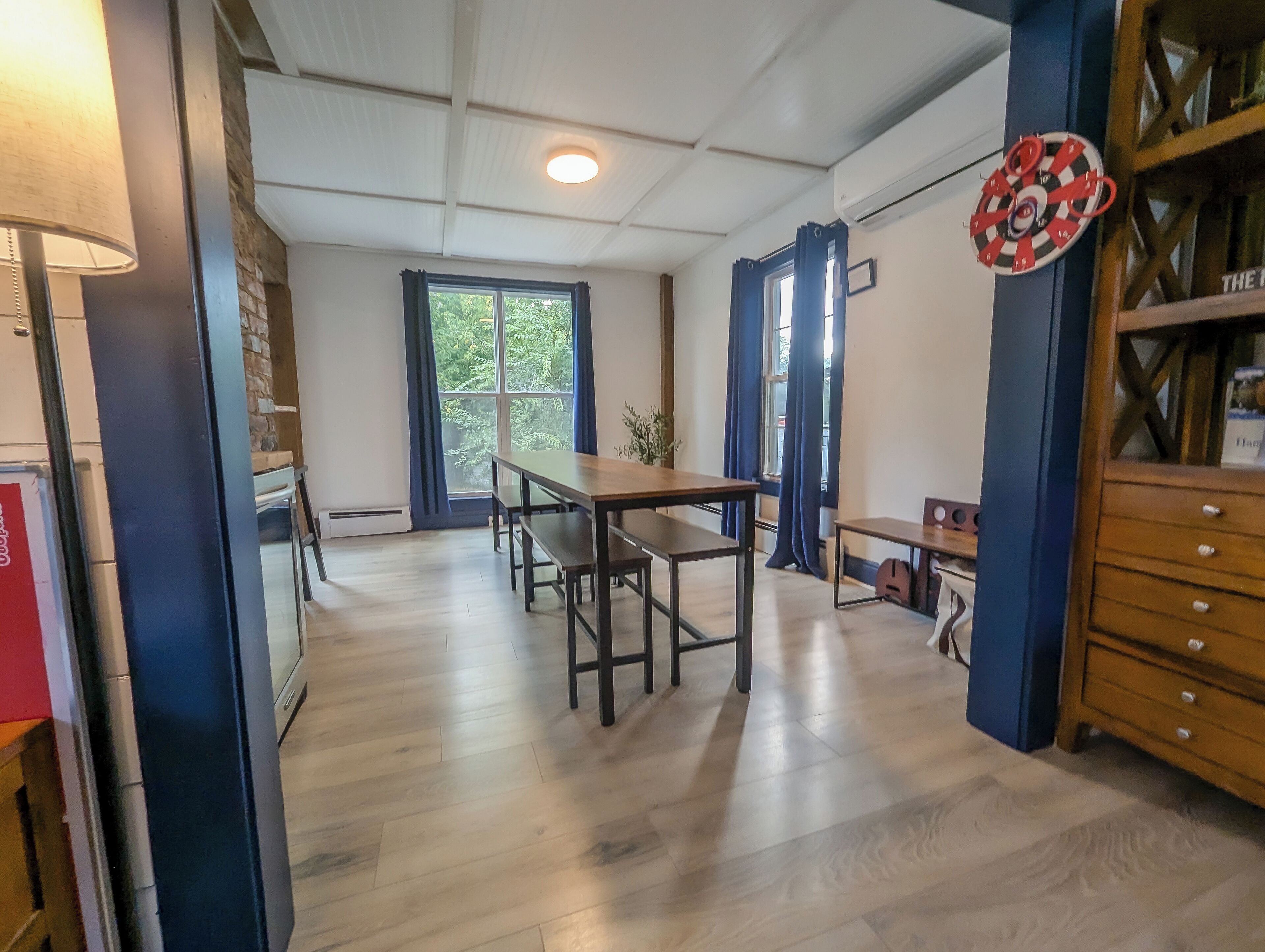 A room with a wooden table and benches, a blue wall unit, and a window with curtains.