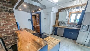 A modern kitchen with a wooden island, blue cabinets, and a brick wall. - Modern Downtown Escape HotTub Fire Pit Games 12ppl (Keene)