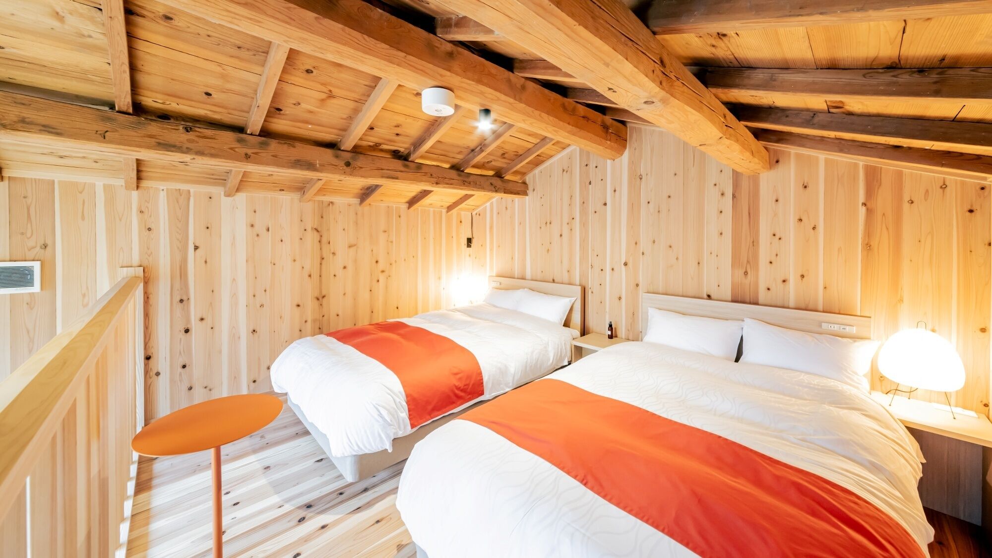 Une chambre dans un chalet en bois, avec deux lits, une petite table et un escalier.