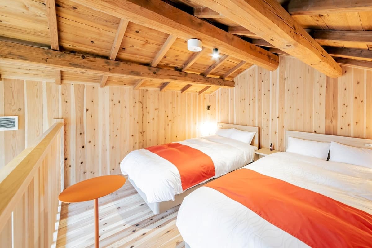 Une chambre dans un chalet en bois, avec deux lits, une petite table et un escalier.