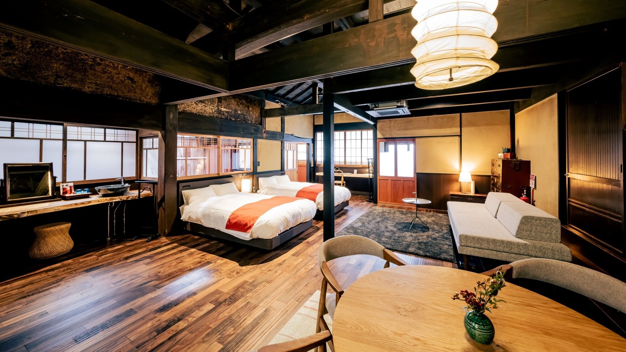 Hotelkamer met houten vloer, twee bedden, een bureau met computer, een bank en een eettafel met vaas.