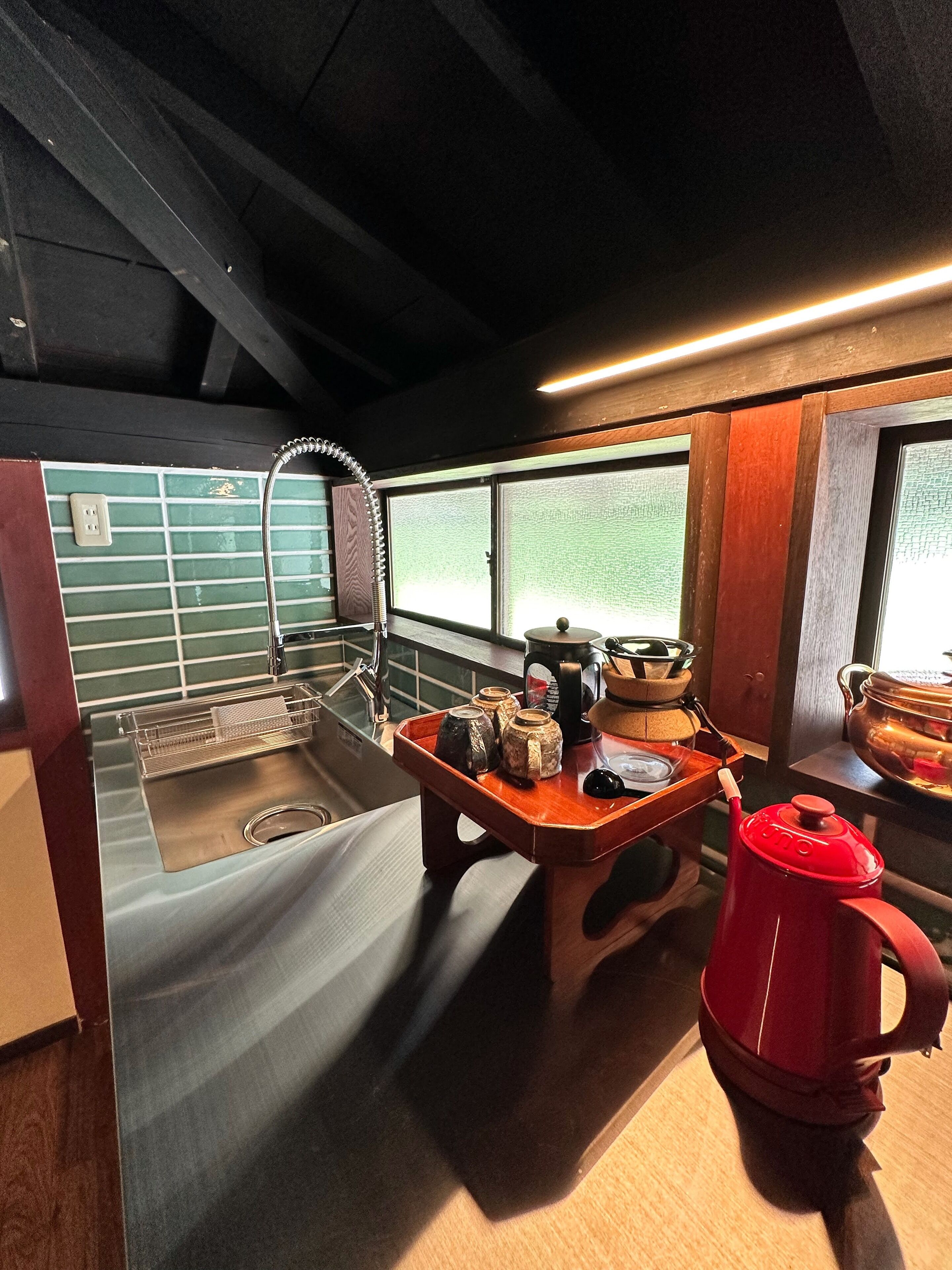 A compact kitchen with a stainless steel sink, wooden countertop, and a red kettle.