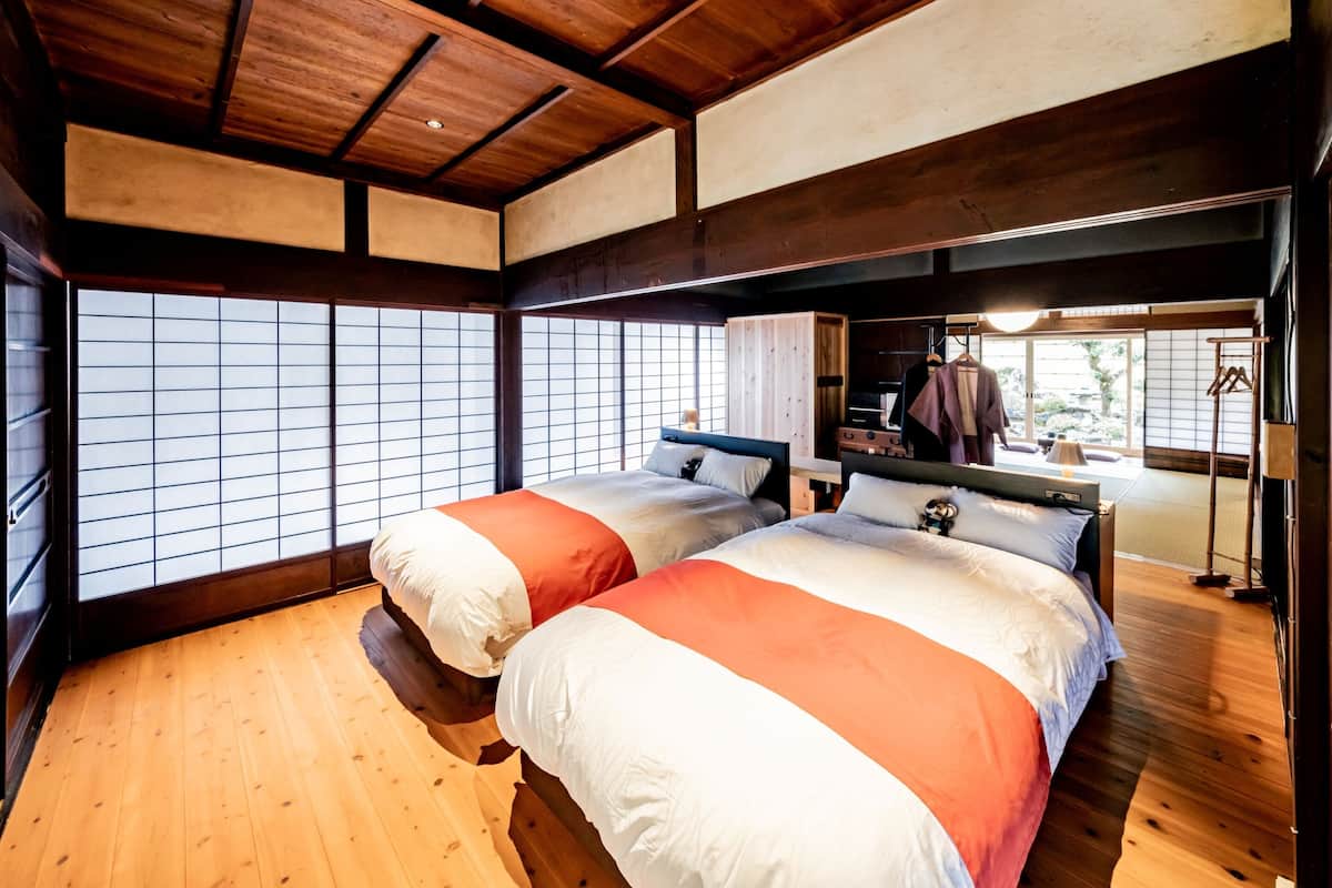 Une pièce de style japonais traditionnel, avec un sol recouvert de tatamis, deux lits avec une literie rouge et blanche, un plafond en bois et une porte coulissante donnant sur un jardin.
