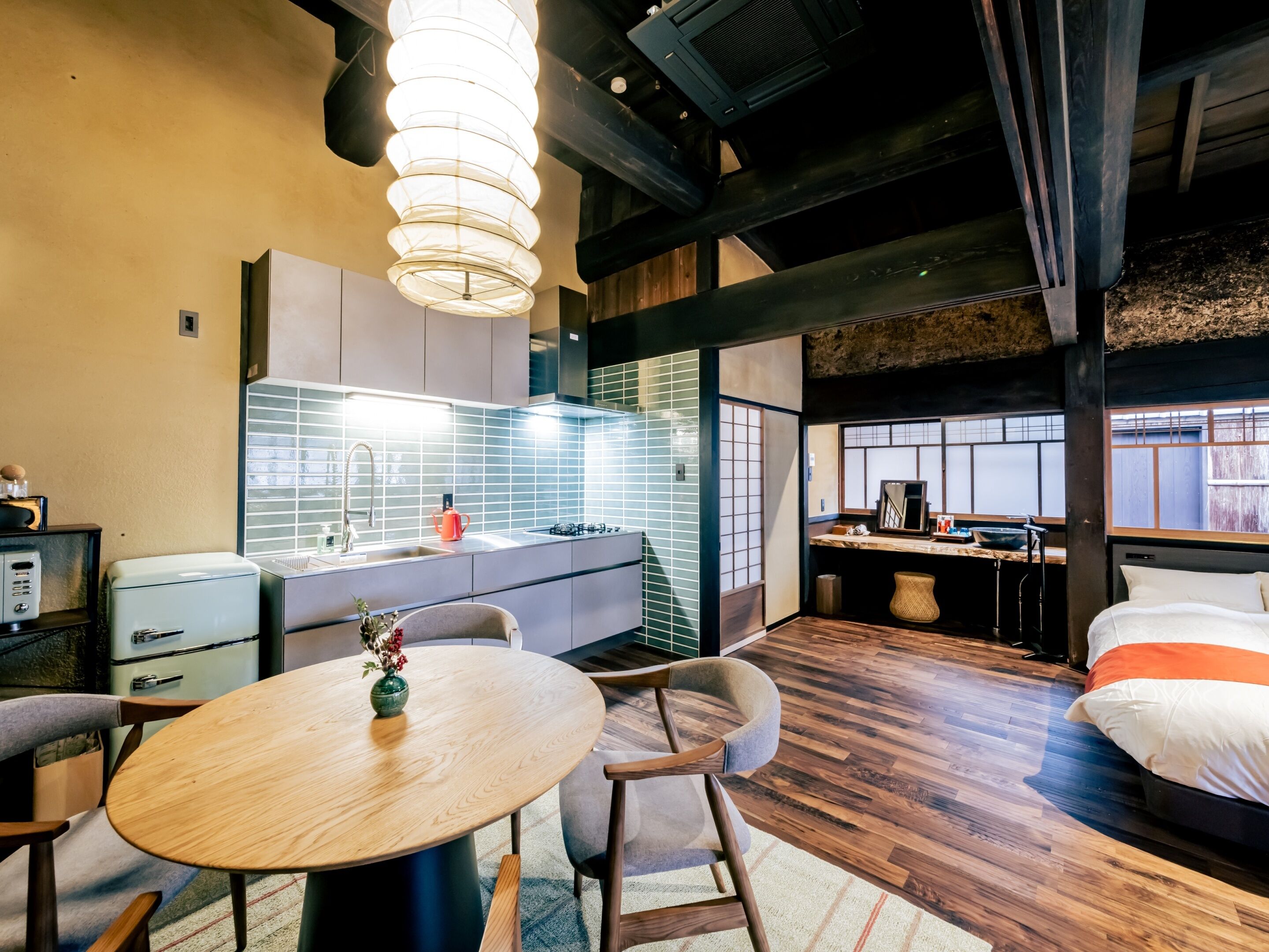 A modern kitchen with a central island, a dining area with a round table, and a bedroom with a bed and window.