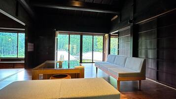 A modern interior with a wooden floor, a sofa, a bed, and large windows offering a view of greenery.