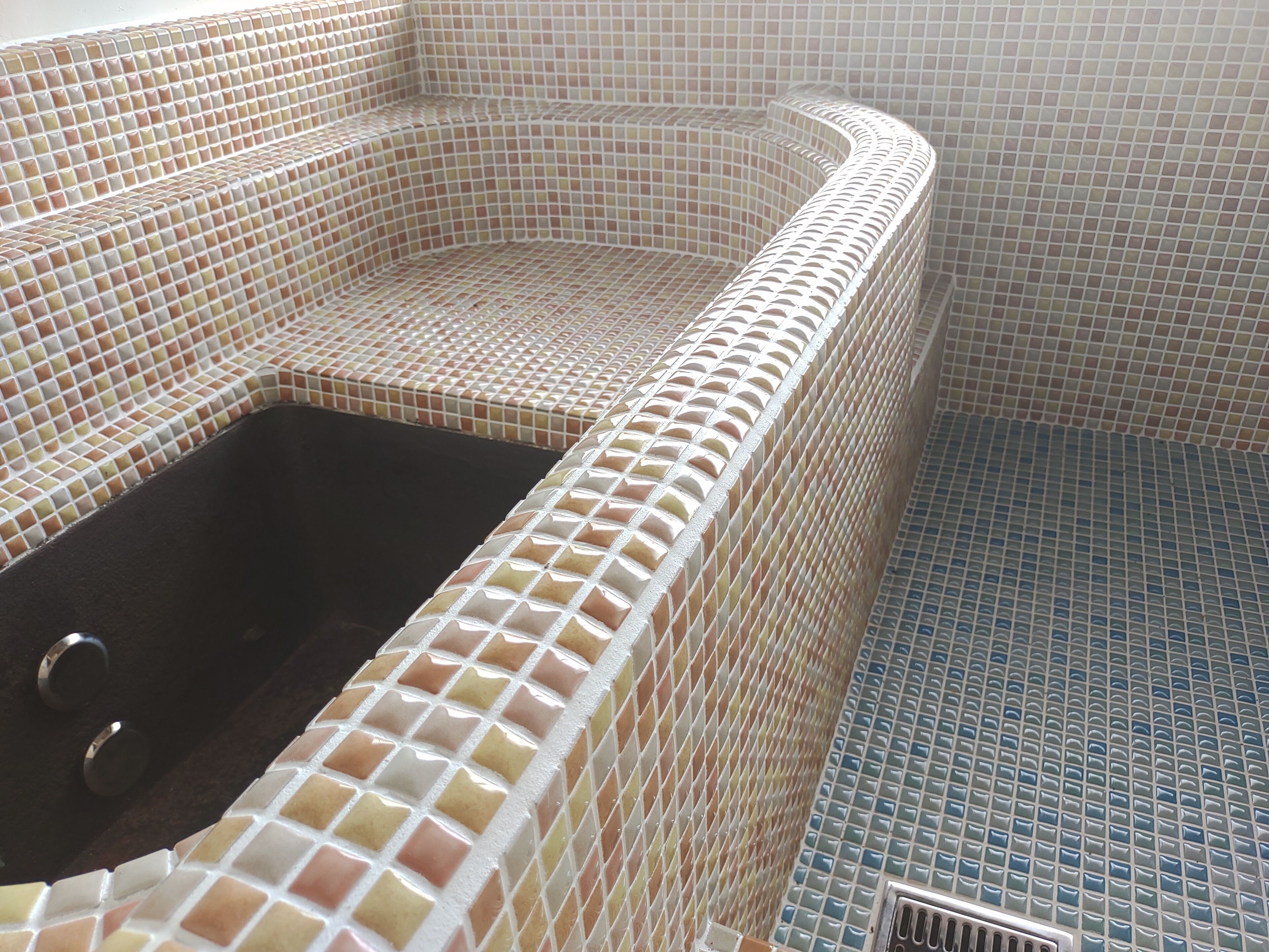 A bathroom with a tiled floor and walls, a bathtub with a drain, and a shower area.