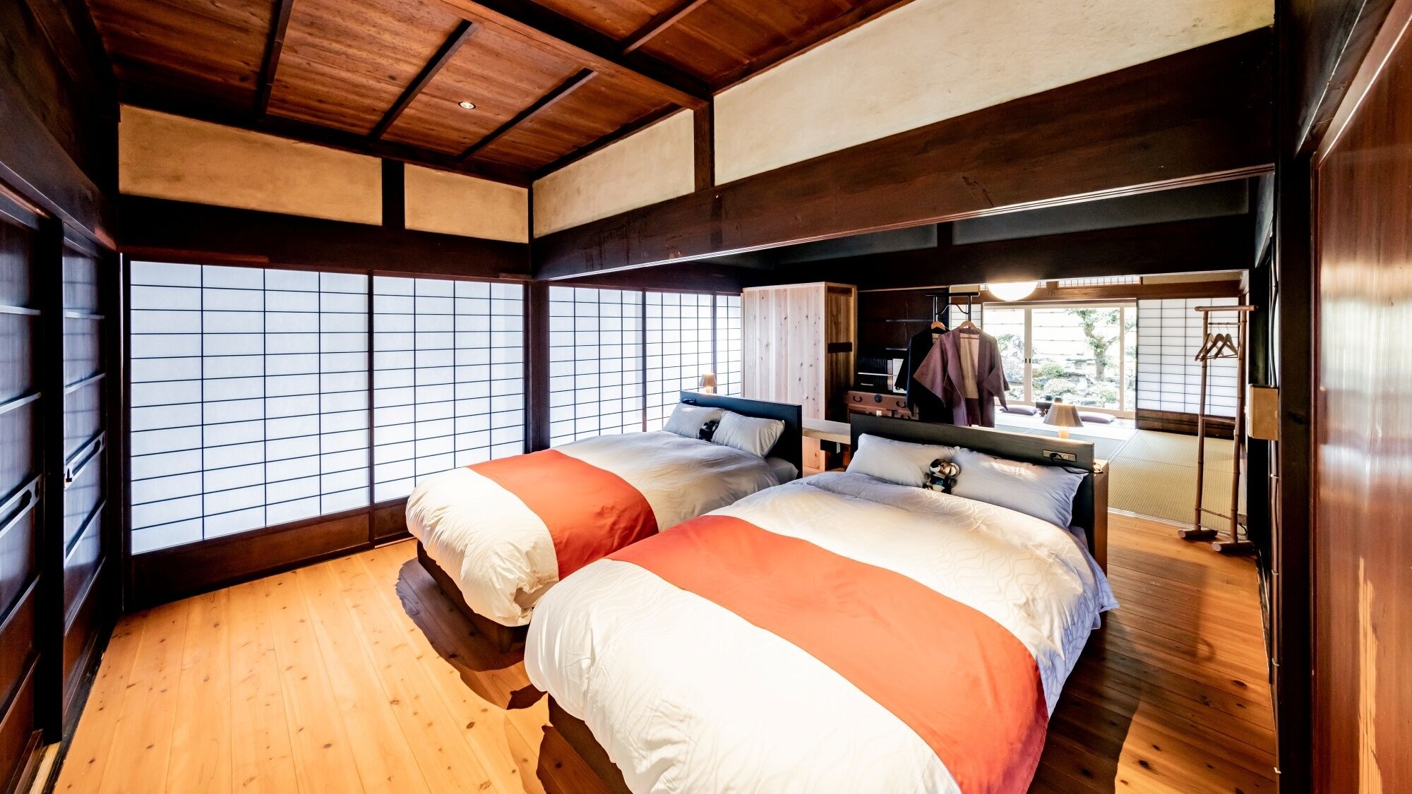 Une pièce de style japonais traditionnel, avec un sol recouvert de tatamis, deux lits avec une literie orange, un plafond en bois et une porte coulissante donnant sur un balcon.