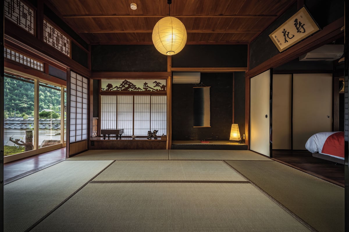 Une pièce traditionnelle japonaise avec un sol recouvert de tatamis, un paravent en papier de riz (shoji), une lanterne en papier suspendue et un futon servant de lit.