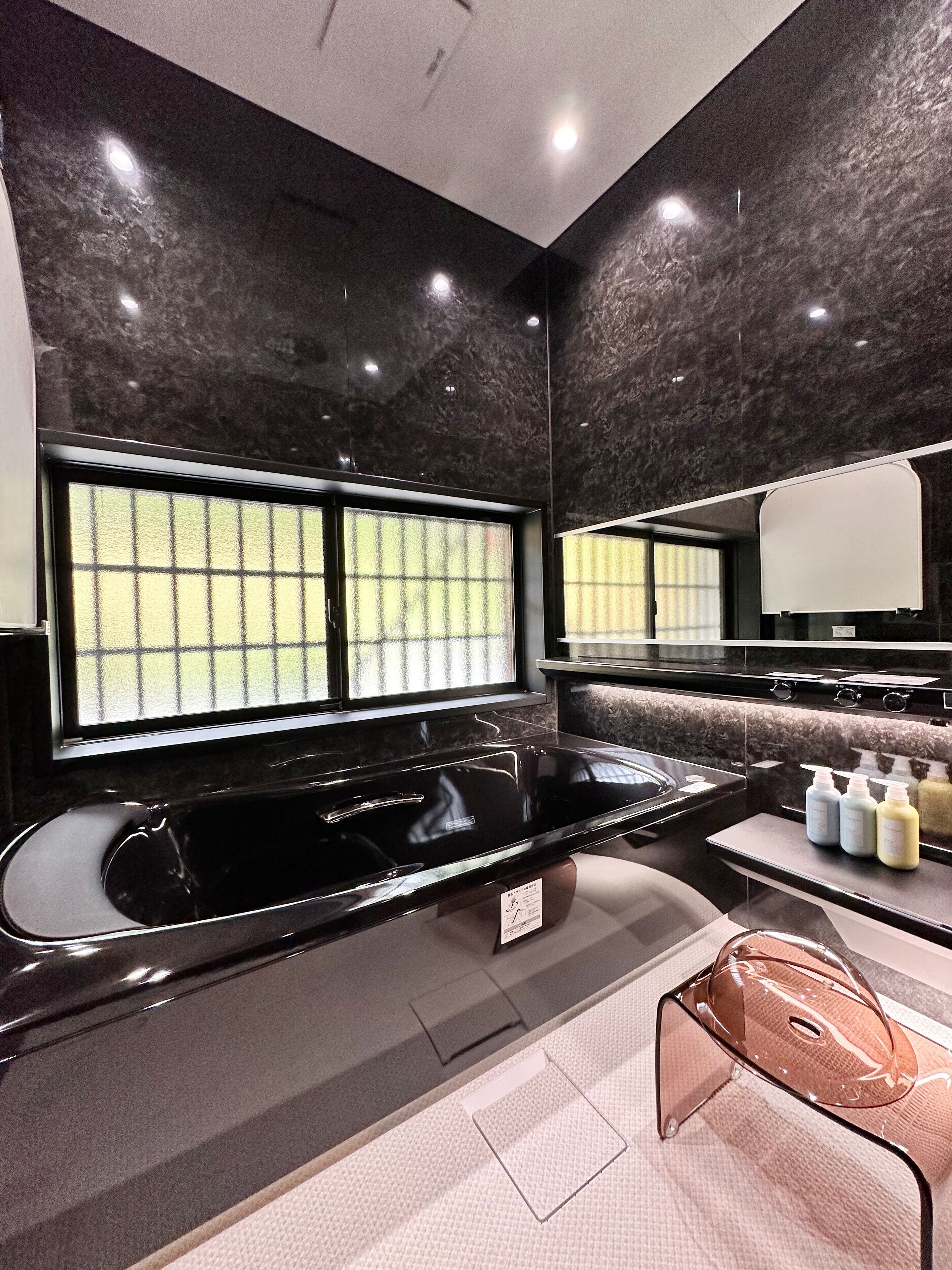 Un baño moderno con encimera de mármol negro, un espejo grande y una ventana con vidrio esmerilado.