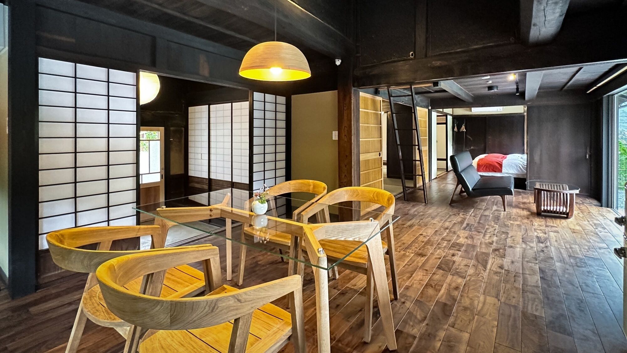 Une pièce de style japonais traditionnel, avec un sol recouvert de tatamis, une table basse et des chaises en bois, une lampe suspendue et des portes coulissantes.