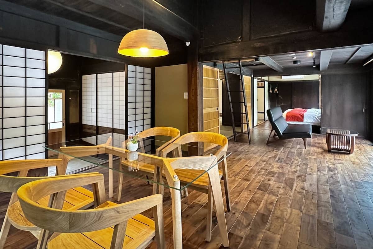 Une pièce de style japonais traditionnel, avec un sol recouvert de tatamis, une table basse et des chaises en bois, une lampe suspendue et des portes coulissantes.