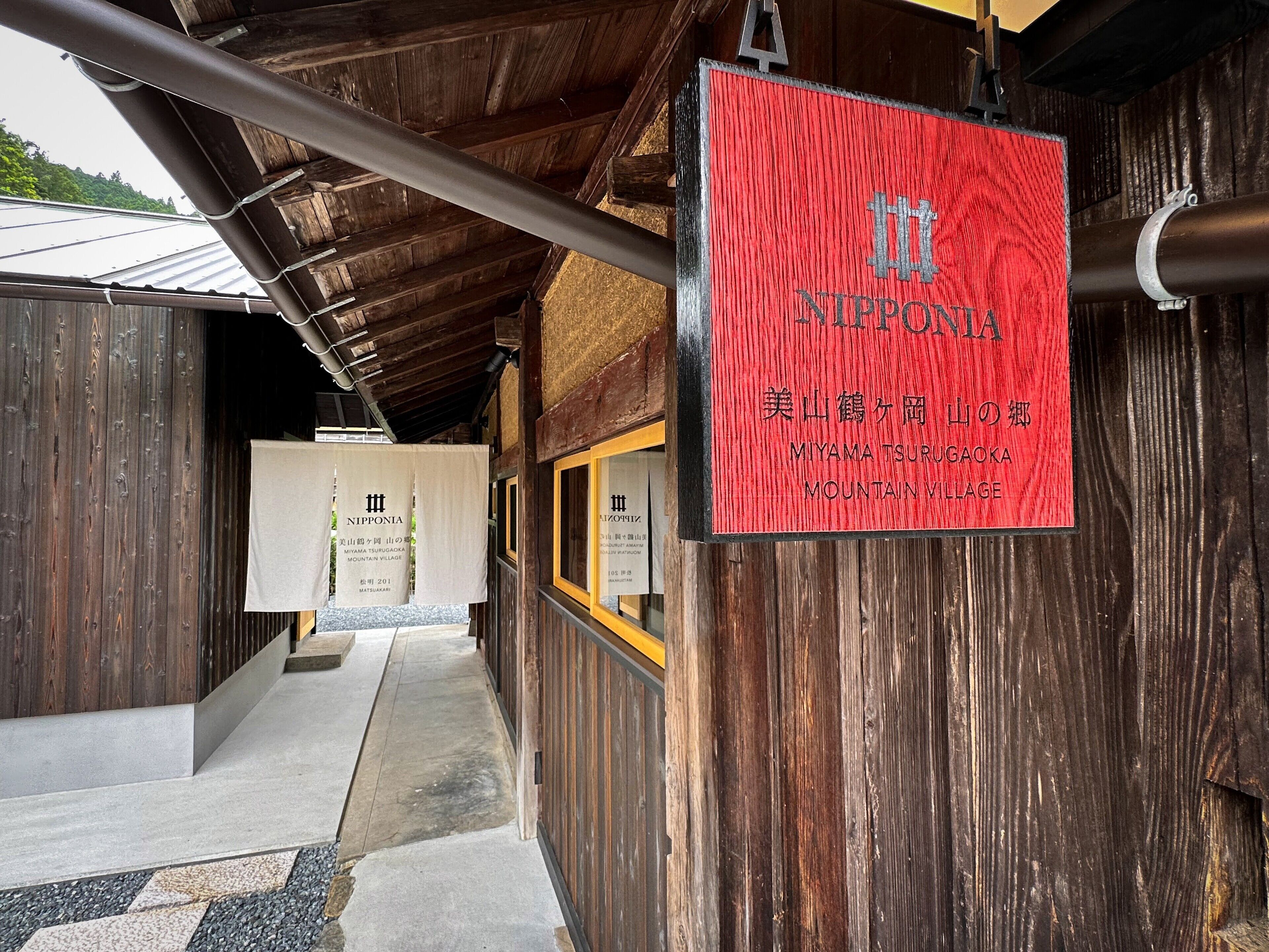 Ein Holzgebäude mit einem roten Schild, auf dem „NIPPONIA MIYAMA TSURUGAOKA MOUNTAIN VILLAGE“ steht.