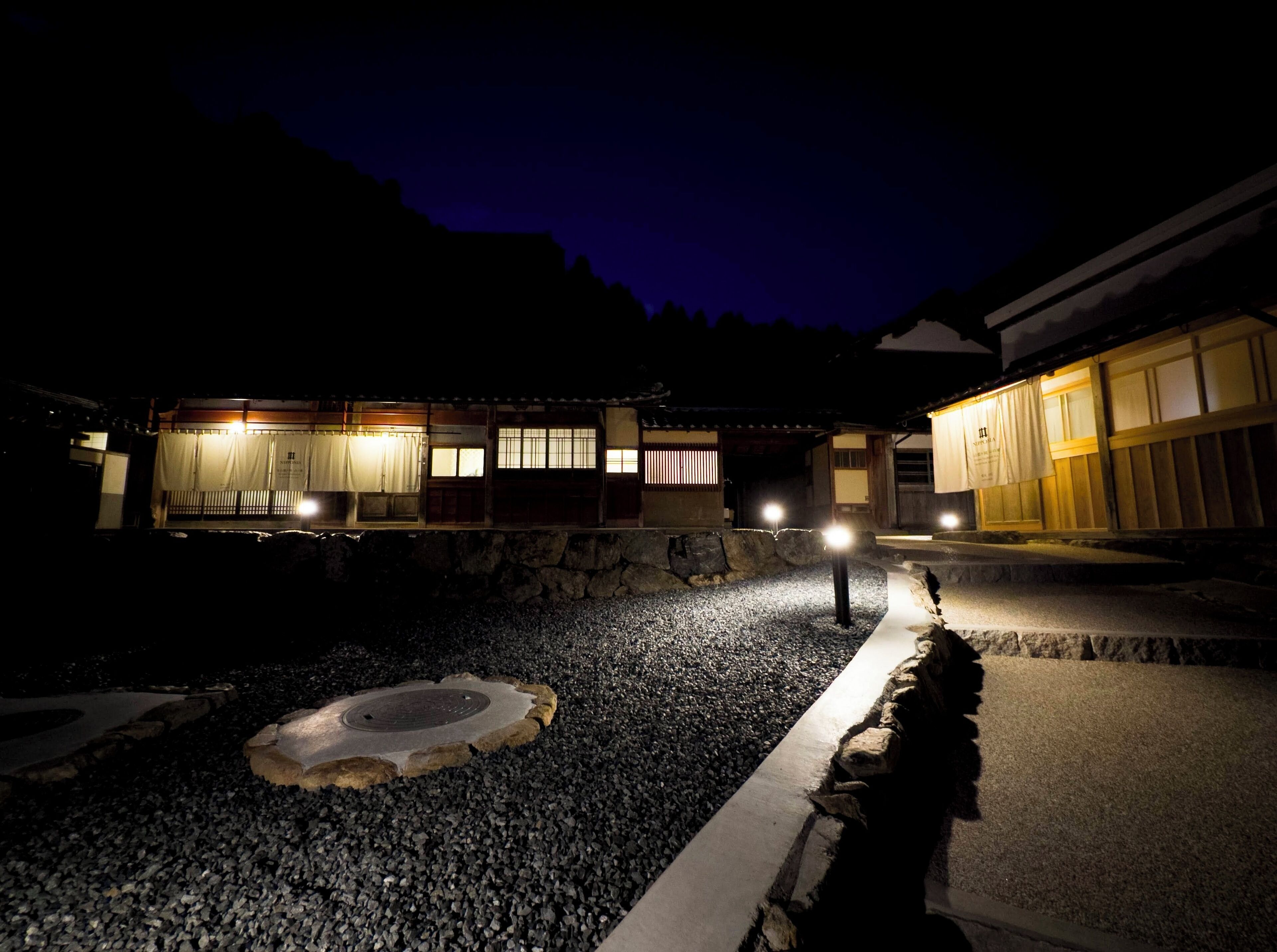 A traditional Japanese building at night with stone pathways and illuminated windows.