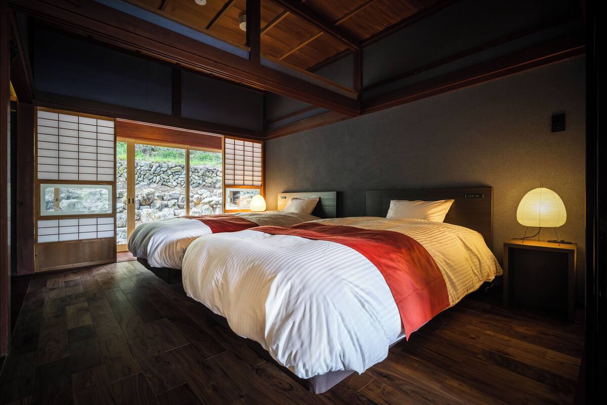 Une chambre de style japonais traditionnel, dotée d’un grand lit, de portes coulissantes de type « shoji » et donnant sur un jardin.