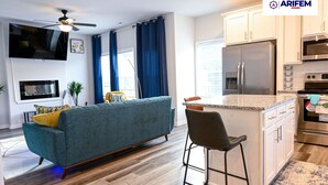 A modern kitchen with stainless steel appliances, a bar stool, and a blue sofa in a living area.