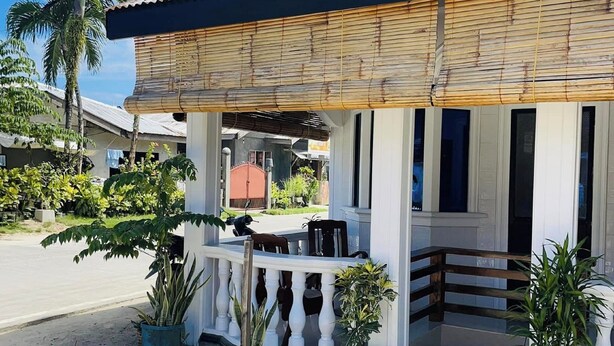 A building with a corrugated metal roof, a covered porch with a wooden railing, and potted plants. - Islescape Siargao (General Luna)