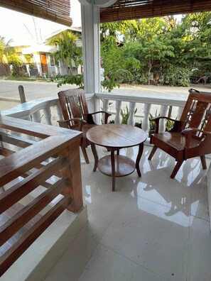 A covered outdoor seating area with a round table and wooden chairs, surrounded by a white railing.