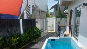 A rectangular pool with a wooden deck in front, surrounded by a low wall and plants. - Islescape Siargao (General Luna)