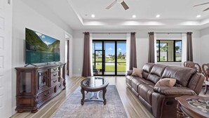 A spacious living room with a large flat-screen TV, leather sofa, and a ceiling fan. - Tranquil location Close to Beaches Lake Front (Rotonda West)