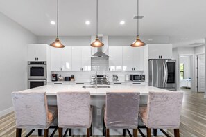Une cuisine moderne avec des meubles blancs, des appareils en acier inoxydable et un îlot central doté de tabourets de bar.