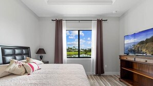 A bedroom with a large bed, a TV on a wooden stand, a window with curtains, and a view of a lake. - Tranquil location Close to Beaches Lake Front (Rotonda West)