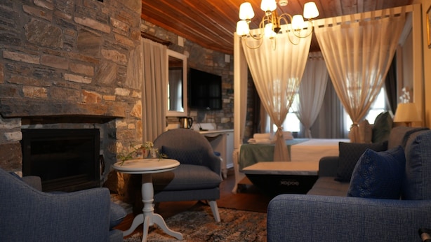 A cozy room with a stone wall, a fireplace, a round table, and a bed with curtains. - Domatia Stone Hotel (Soke)