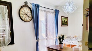 A room with a large wall clock, a chandelier, a dining table with chairs, and a window with curtains. - Vacation home - Tourist rental "Belvedere House Holiday Syracuse Ortigia" (Siracusa)