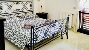 A bedroom with a bed, a bedside table, a hanging light fixture, and a window with curtains. - Vacation home - Tourist rental "Belvedere House Holiday Syracuse Ortigia" (Siracusa)