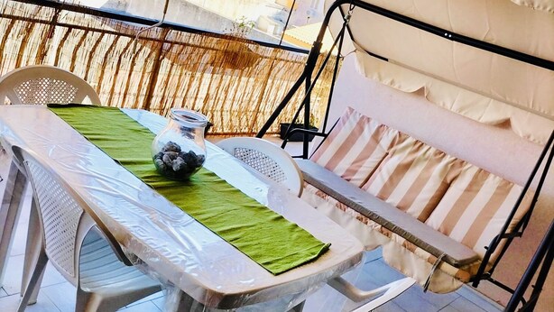 A balcony with a table set for two, a cushioned bench, and a view of buildings in the background. - Vacation home - Tourist rental "Belvedere House Holiday Syracuse Ortigia" (Siracusa)